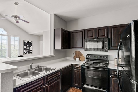 a kitchen with black appliances and white counters and dark wood cabinets at Veranda at Centerfield in Houston, Texas 77070